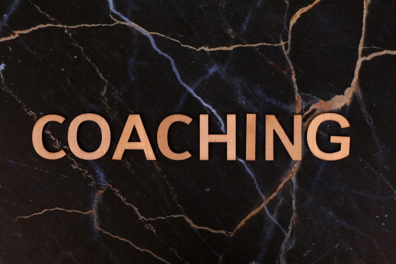 heros-img Wooden letters spelling 'Coaching' on dark marble surface, emphasizing guidance and mentorship.